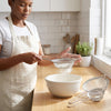 A person using a Stainless Steel Mesh Strainer Filter Spoon to sift flour into a bowl in a bright kitchen.