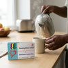 Pouring hot water into a mug with Anti-Heart Failure Herbal Tea box on the table.