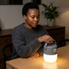 Woman using a Solar Rechargeable LED Camping Light on a table in a cozy setting.