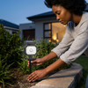 A woman installing a Multifunctional Solar Wall Lamp in her garden for enhanced outdoor lighting.