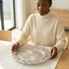 A woman placing a 13-inch Eco-Friendly Charger Plate on a dining table, showcasing its elegant design.