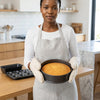 Woman in apron holding a cake in a round pan in a kitchen, using a 3 Piece Non Stick Bakeware Set.