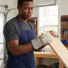 A man wearing Heat Resistant Anti-Chemical Leather Working Gloves while working on a wooden plank in a workshop.