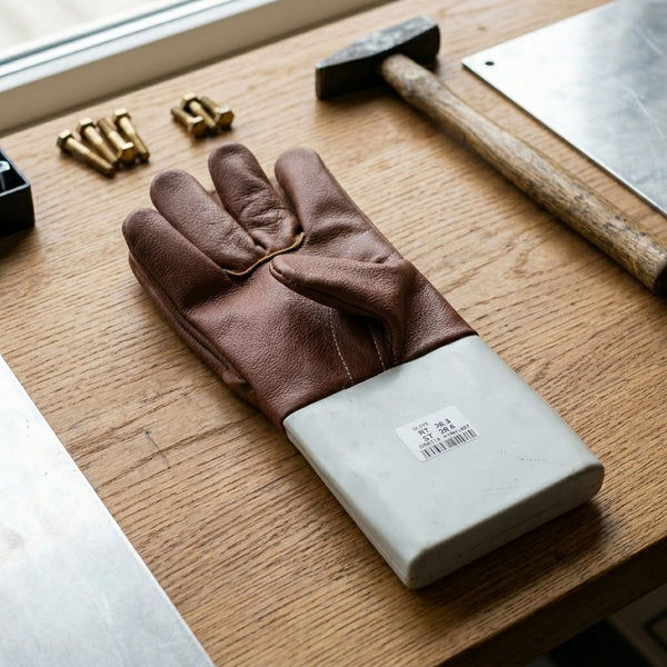 Reinforced Leather Safety Gloves placed on a wooden table next to tools and equipment for protection in manual work.