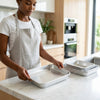 Woman in a kitchen holding a tray from the 3-Piece Aluminum Nesting Oven Tray Set on a countertop.