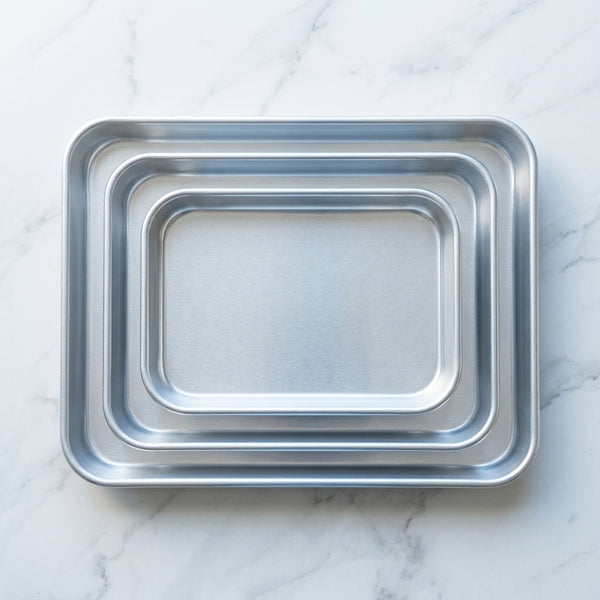 3-Piece Aluminum Nesting Oven Tray Set displayed on a marble surface, showcasing space-saving design.