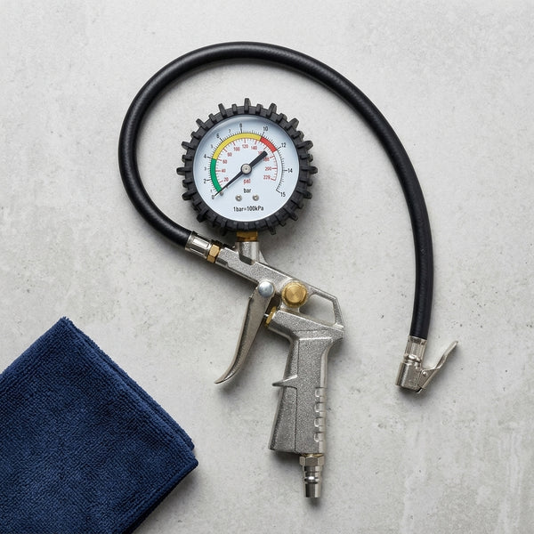 Car Tyre Pressure Gauge showing pressure readings with a silver handle and black hose on a grey surface.