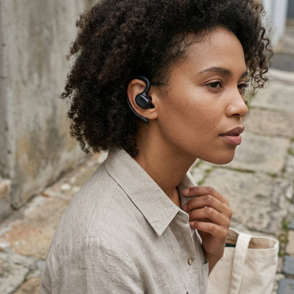 X27 Air Conduction True Wireless Earbuds worn by a woman with curly hair outdoors.