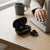 X58 TWS Wireless Ear Clip Sports Headphones in charging case on a wooden table with a laptop and coffee cup.