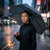 A person holding a stylish heart-patterned umbrella while standing in the rain, showcasing the 21-Inch Automatic Foldable Windproof Umbrella.