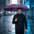 Man holding an Auto Open 3-Folding Portable Umbrella in the rain on a city street.