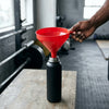 Person using a 250mm Large Multipurpose Food Grade Plastic Funnel to pour liquid into a black bottle in a gym setting.