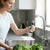 Woman using the 360 Degree Rotating Faucet Anti-Splash Filter to wash vegetables in a kitchen sink.