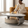 Woman in cream outfit placing a cup on a Marble Finish Top Coffee Table in a modern living room.