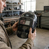 Person holding a German Style Auto Darkening Welding Helmet in a workshop setting, showcasing its reflective visor.