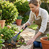 Woman using Metal Garden Lawn Rake with Telescopic Handle to tidy flower beds in a garden.