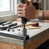 Hand using a drill with EXTREME Impact Pivoting Bit Tip Holder on metal workpiece, showcasing versatility in tight spaces.
