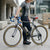 Single Speed Aluminium Alloy Fixed Gear Bike parked by a cyclist in a city setting, showcasing its sleek design and lightweight build.