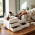 A hand organizing cosmetics in a Double-Layer Cosmetics Storage Box on a wooden vanity.