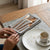 Modern Slim Handle Stainless Steel Cutlery elegantly arranged on a grey napkin on a wooden table beside a coffee cup.