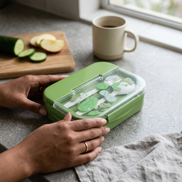 Person holding a 3 Compartment BPA Free Microwave Bento Lunch Box in green with vegetables on a countertop.