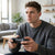 A man seated in a living room playing with a PS3 Wired Joystick Game Controller, focused and engaged.