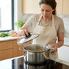 Woman lifting lid off Stainless Steel Round Stock Pot with Lid while cooking soup in a modern kitchen.