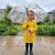 Child holding a colorful Reinforced Transparent Windproof Long Handle Umbrella while wearing a yellow raincoat in the rain.