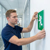 A man installing an Aluminum Emergency Direction Arrow Sign on a wall for evacuation guidance.