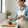 Woman using a Velvet-Touch Pastel Precision Knife to cut a red bell pepper on a wooden cutting board in a kitchen.