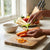 Person using a peeler on carrots with the 3-Piece Stainless Steel Vegetable Peeler Set in a well-lit kitchen.