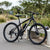 Enduro Mountain Bike with Aluminum Frame and Disc Brakes on a pathway surrounded by greenery.