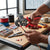 A person using Tubular Terminal Crimping Pliers to secure electrical connections at a workbench with tools and accessories.