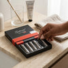 Pack of 6 Premium Durable Sharp Nail Clipper in a sleek box on a countertop next to hand cream and a hand reaching for clippers.