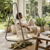 Woman relaxing in a Macrame Hanging Hammock Chair with Steel Stand indoors, surrounded by greenery.