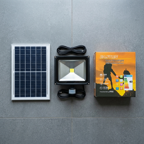 30W Solar Floodlight with Motion Sensor, solar panel, and packaging displayed on a gray surface.
