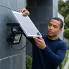 Man installing 30W Solar Floodlight with Motion Sensor on wall, adjusting solar panel for optimal sunlight exposure.