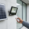Person using remote to operate a 100W Solar Floodlight mounted next to a solar panel.