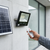 Person using remote to operate a 100W Solar Floodlight mounted next to a solar panel.