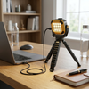 Portable LED Work Light with Adjustable Tripod Stand on a desk next to a laptop and a notebook.