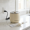 Mini Rice Cooker on countertop with rice, measuring spoon, and instruction booklet for easy cooking.