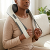 Person using a Wearable Shoulder and Neck Massager while sitting on a couch in a cozy environment.