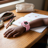 Hand wearing a pink Transforming Robot Digital Watch on a wooden table with colorful pencils and a notebook.
