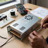 12V 50A Fan-Cooled Switching Power Supply on a wooden table with tools and wires for electrical projects.