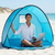 A woman sitting inside a Two Person Beach Tent on the sand, working on a laptop, enjoying a sunny beach day.