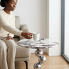 A person placing a cup on the Luna Marble-Look Round Side Table in a modern living space.