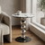 Round Marble-Look Coffee Table with Decorative Metal Base beside a couch and window, featuring a coffee mug on top.