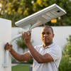 A man adjusting an 80W Solar Street Light with a solar panel outdoors in a well-lit garden setting.