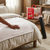 Portable Electric Heated Blanket on a bed with a person’s hand resting on it, showcasing the product packaging.