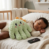 Plush Electric Soothing Dinosaur Massager Cushion & Remote beside a sleeping baby on a bed.
